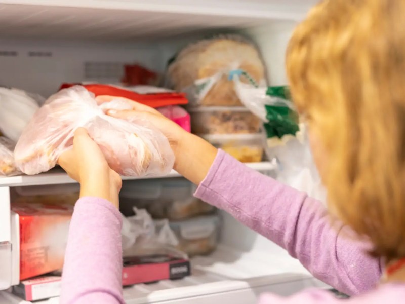 Junge Frau holt Päckchen mit gefrorenem Fleisch aus dem Froster