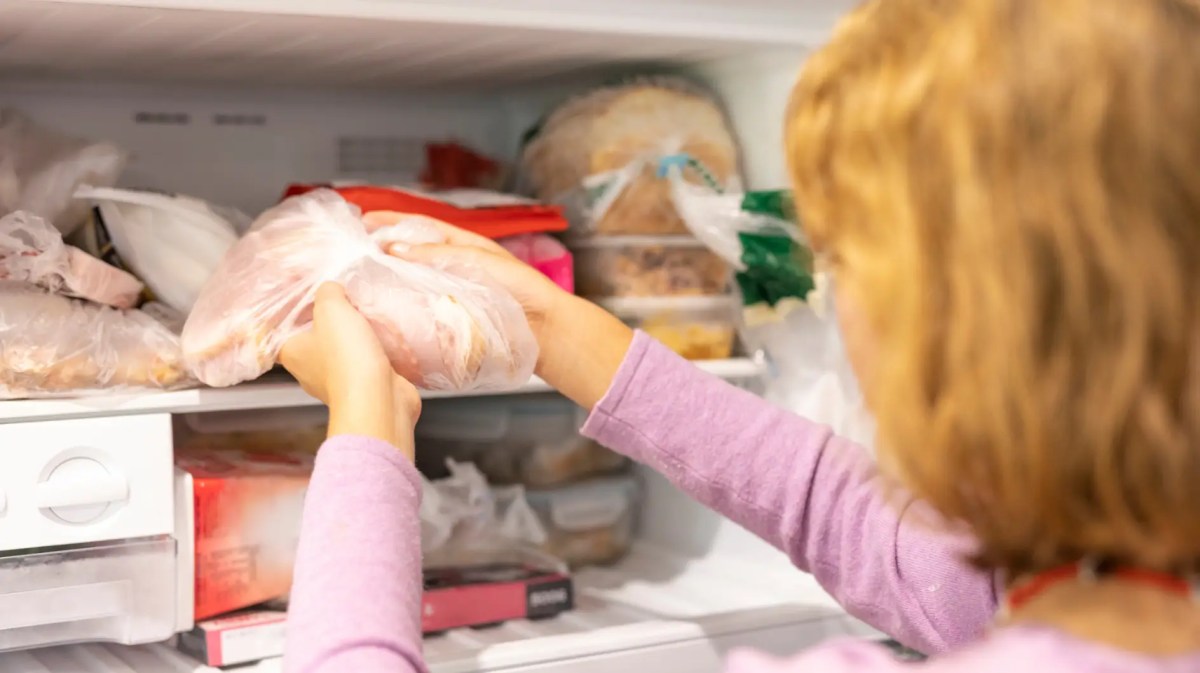 Junge Frau holt Päckchen mit gefrorenem Fleisch aus dem Froster
