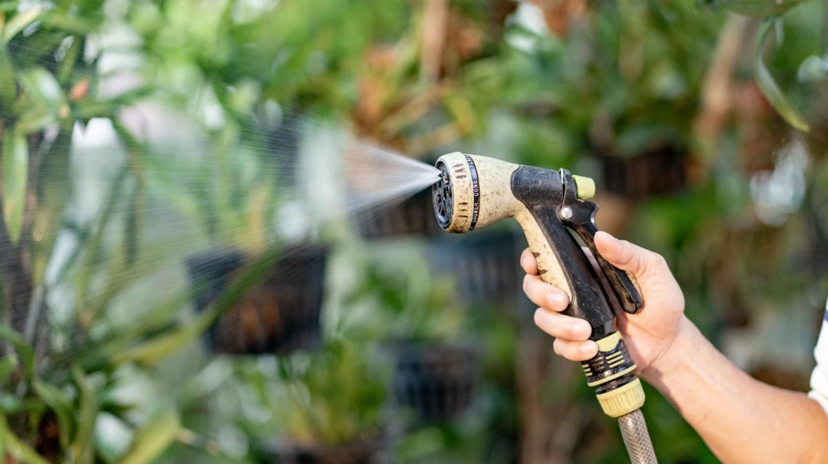 Frau hat einen Gartenschlauch mit Düse in der Hand, aus der Wasser kommt.