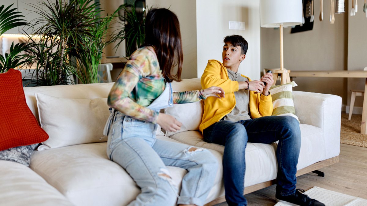 Bruder und Schwester sitzen nebeneinander auf dem Sofa und streiten um die Fernbedienung.