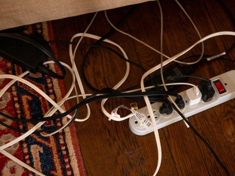 Auf dem Boden liegen verschiedene Kabel, die in einer Mehrfachsteckdose stecken und chaotisch ineinander verwoben sind.