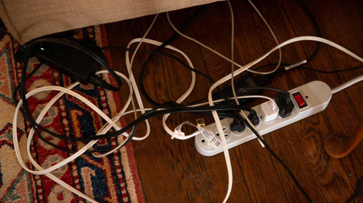 Auf dem Boden liegen verschiedene Kabel, die in einer Mehrfachsteckdose stecken und chaotisch ineinander verwoben sind.