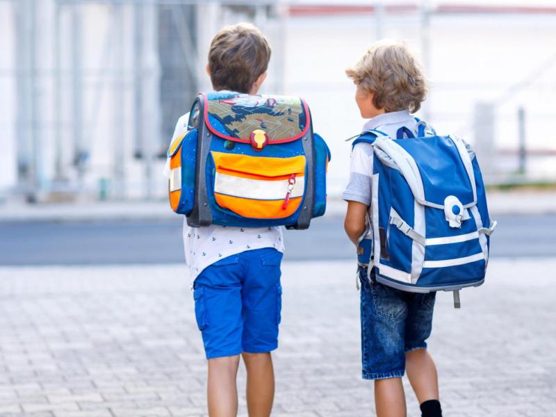 zwei Jungs mit Schulranzen gehen drau&szlig;en gemeinsam.
