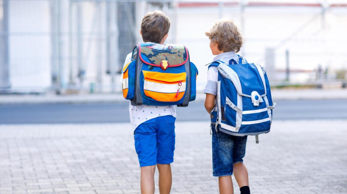 zwei Jungs mit Schulranzen gehen draußen gemeinsam.