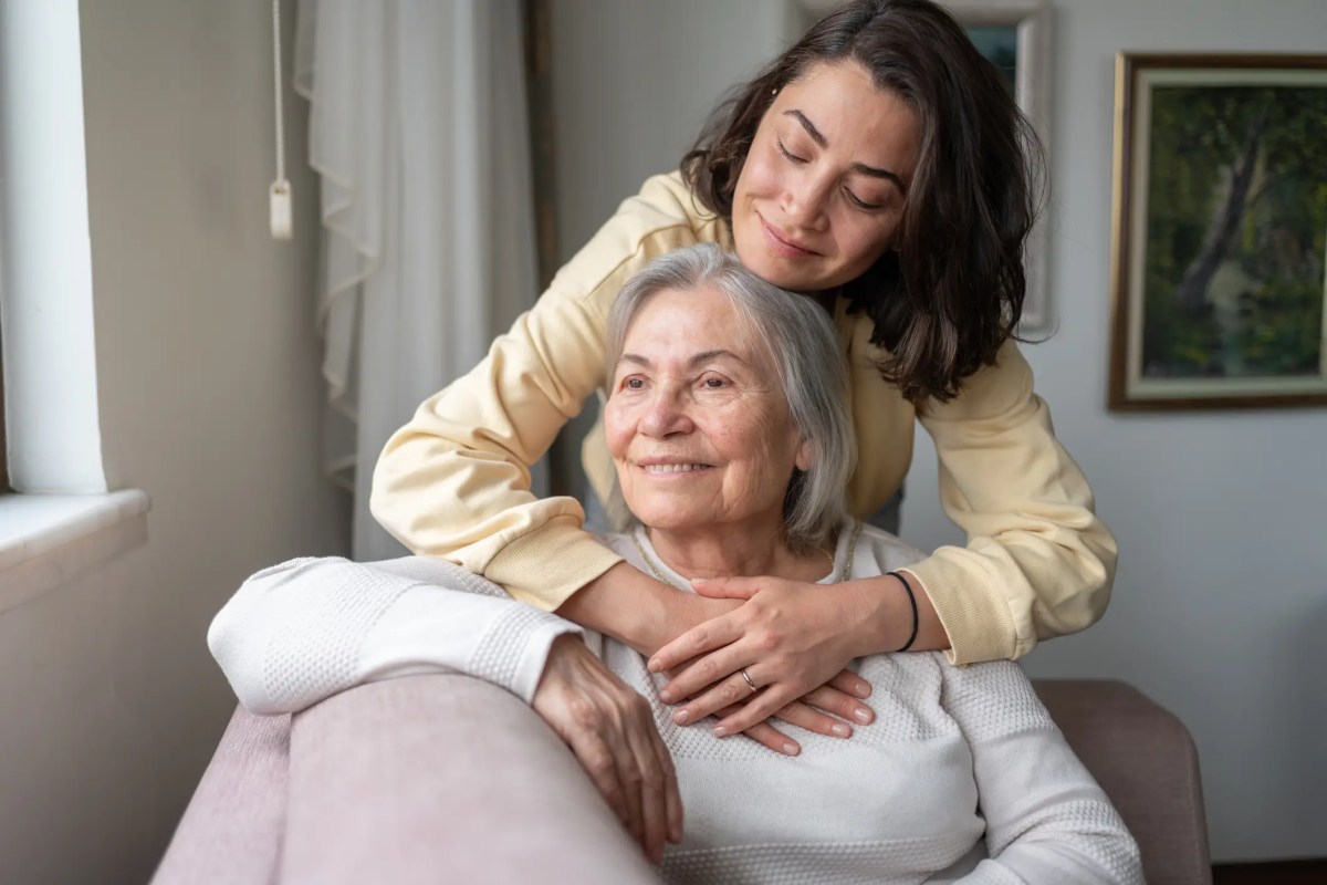 Junge Frau umarmt ihre ältere Mutter auf der couch.