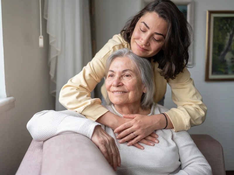 Junge Frau umarmt ihre ältere Mutter auf der couch.