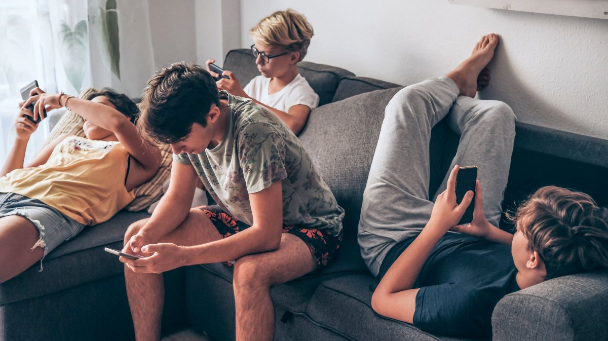 Vier Teenager hängen auf dem Sofa ab, all mit dem Handy in der Hand.