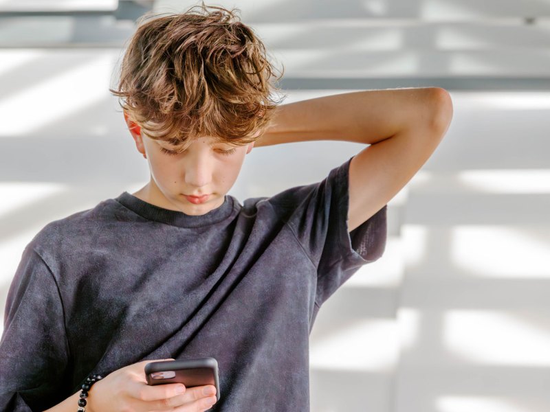 Teenager schaut nachdenklich auf sein Handy.