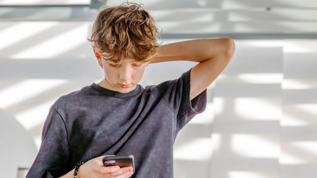 Teenager schaut nachdenklich auf sein Handy.