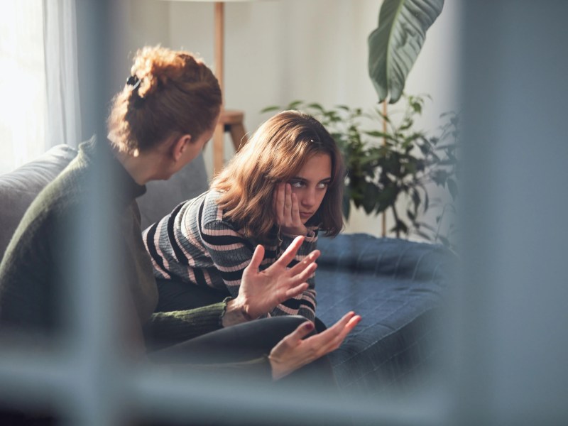 Teenager-Mädchen sitzt verärgert mit Mutter auf der Couch.