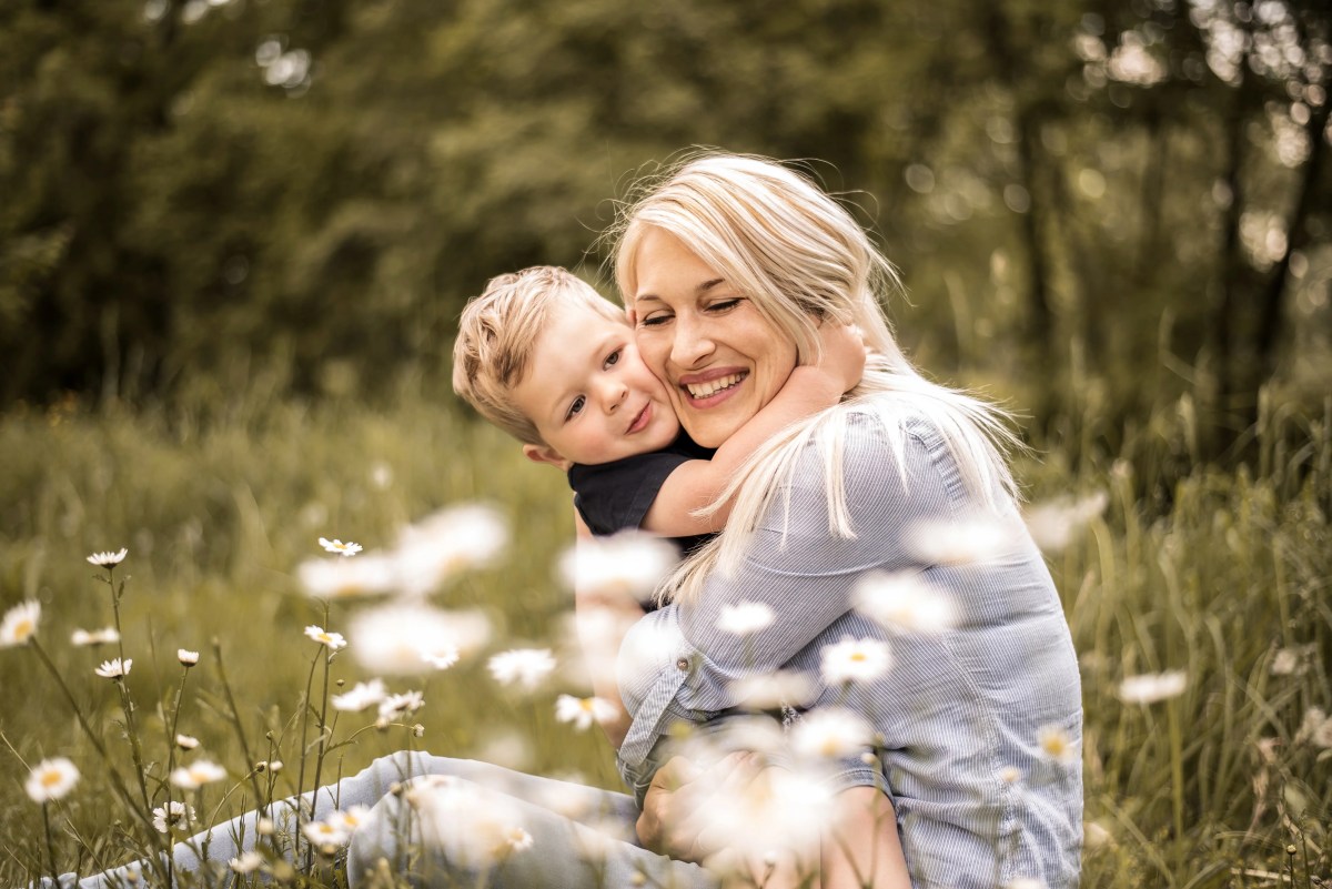 Blonde Mutter sizt glücklich umarmend mit ihrem Klienkind in einer Blumenwiese