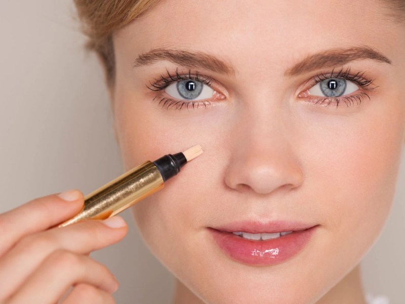 Frau, die einen Concealer unter dem Auge aufträgt.