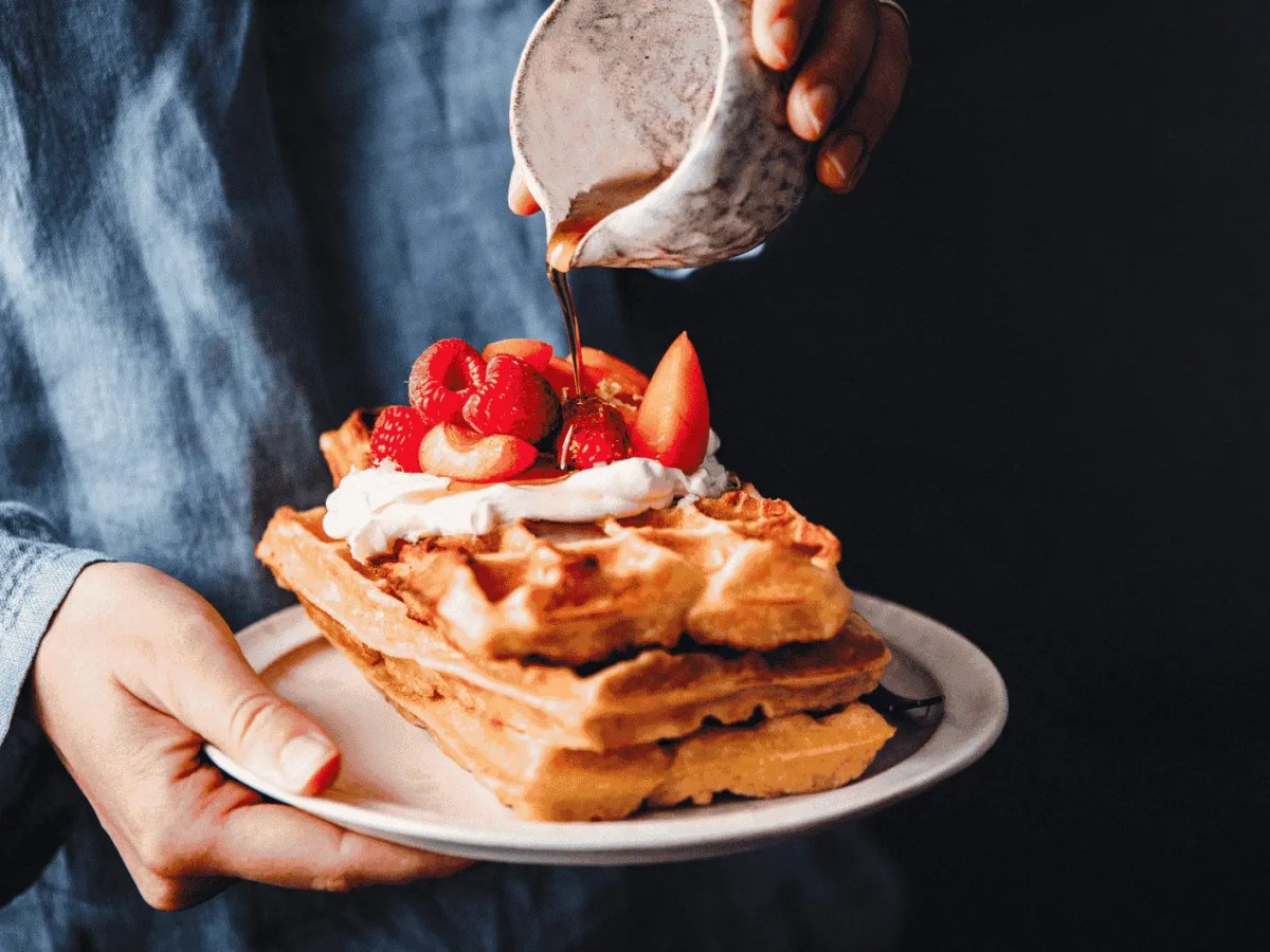 Frau gießt Sirup auf frische Waffeln mit Erdbeeren.