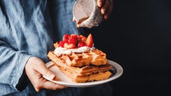 Frau gie&szlig;t Sirup auf frische Waffeln mit Erdbeeren.