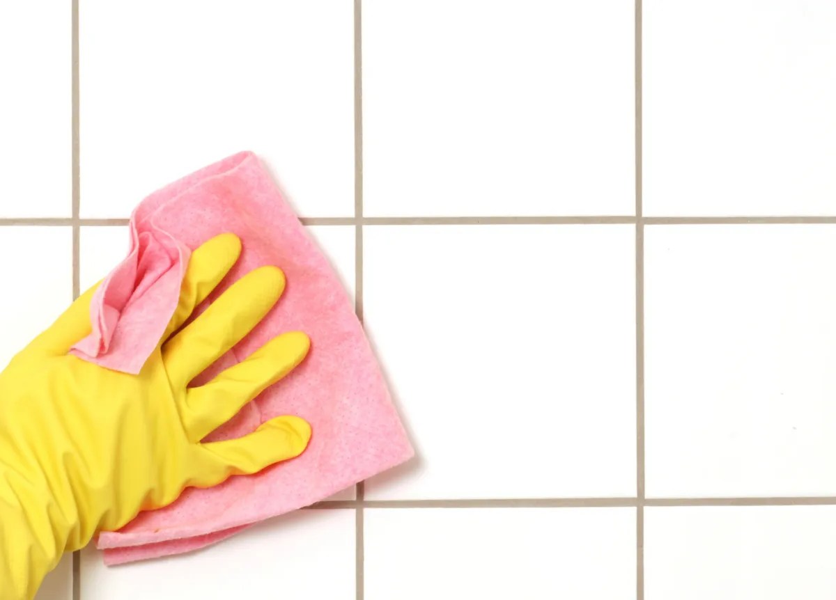 Person wischt mit rosa Lappen &uuml;ber Fugen in Badezimmer.
