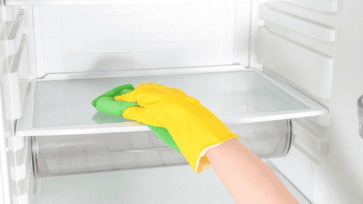 Person mit gelbem Reinigungshandschuh wischt durch Kühlschrank.
