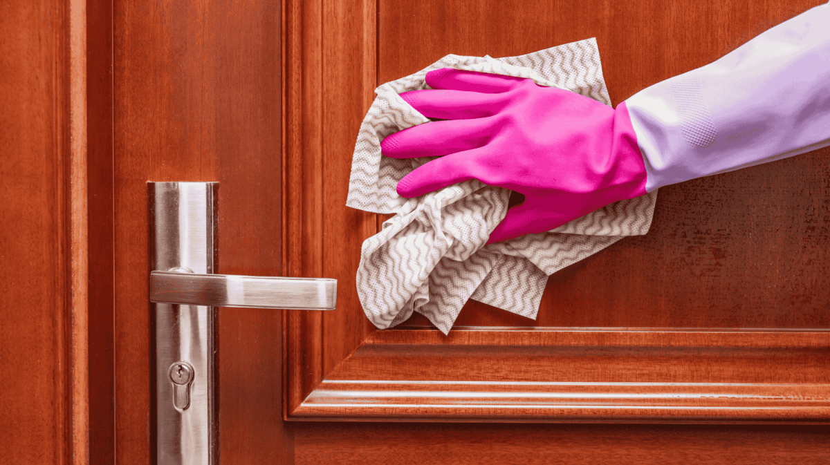 Person mit pinkem Putzhandschuhe wischt mit Lappen über Wohnungstür.