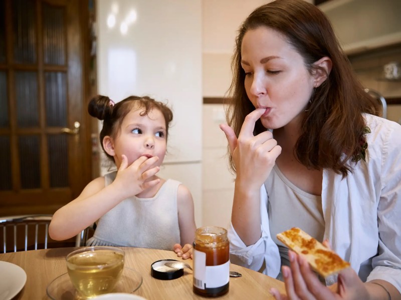 Mutter und Tochter sitzen am Küchentisch und essen Brot mit Marmelade