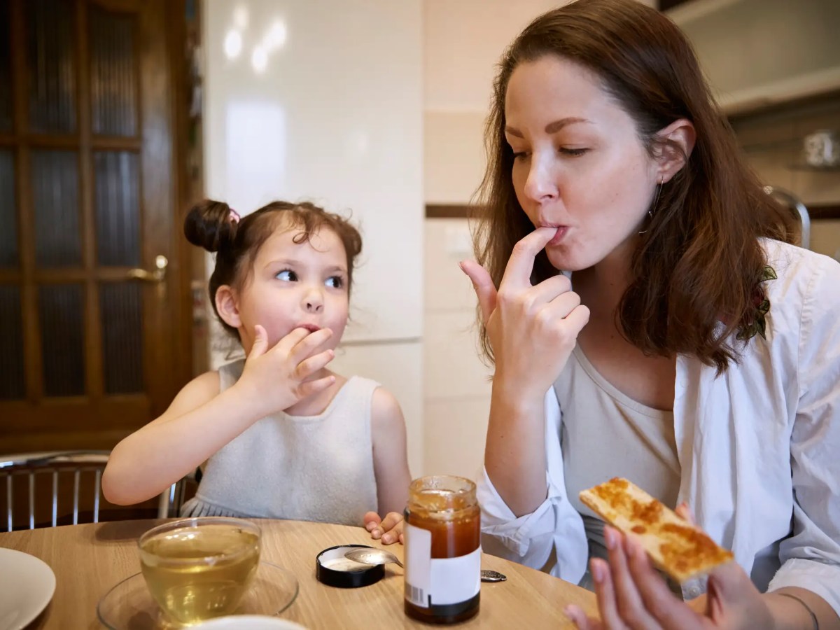 Mutter und Tochter sitzen am Küchentisch und essen Brot mit Marmelade