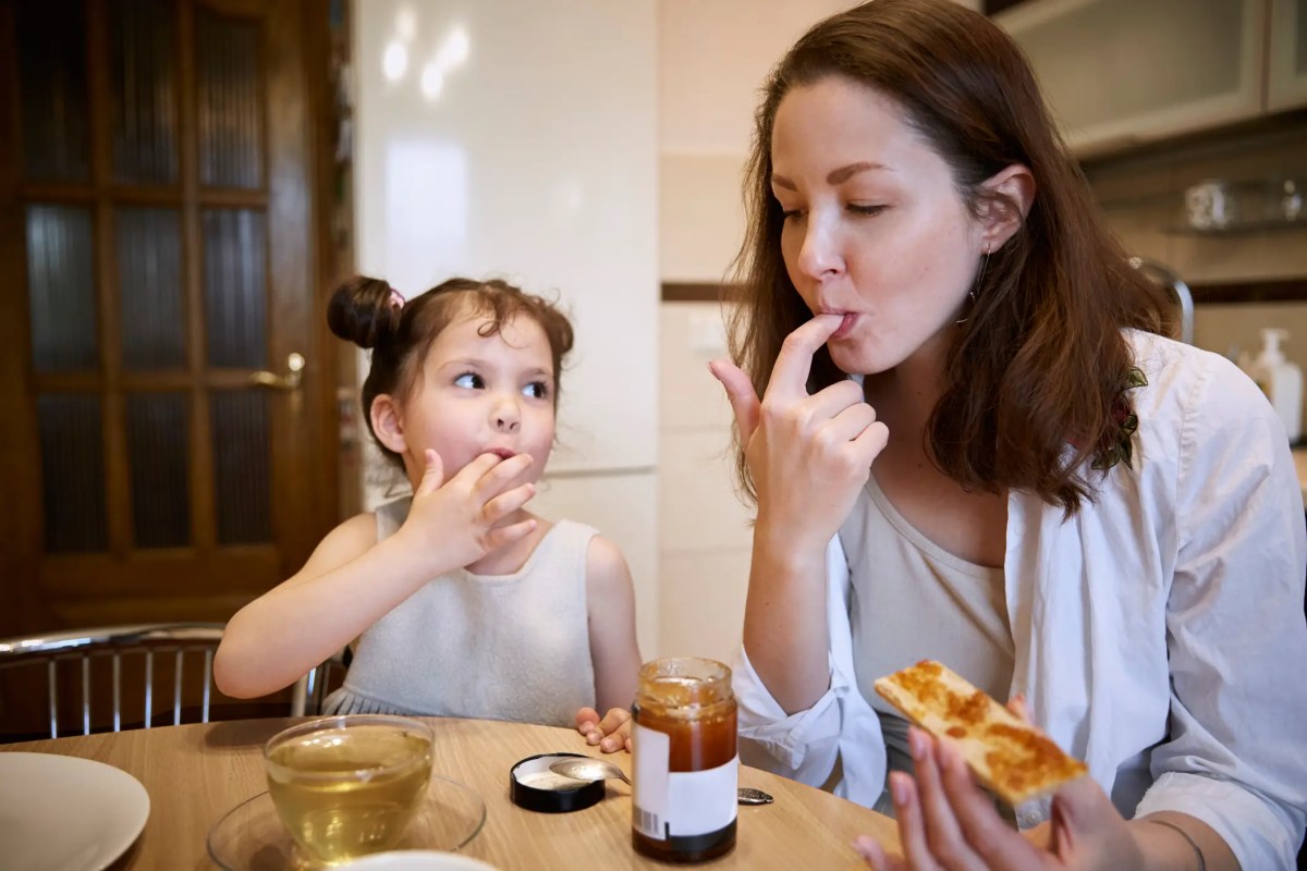 Mutter und Tochter sitzen am Küchentisch und essen Brot mit Marmelade