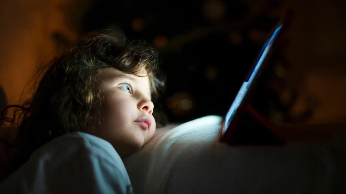 Kind, ca. 4 Jahre, sitzt im Dunkeln gebannt und ganz nah vor einem Tablet-Bildschirm.