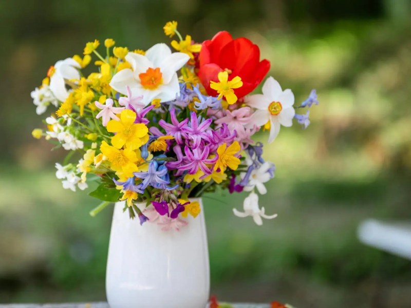 Verschiedene Wildblumen in einer wei&szlig;en Vase stehen drau&szlig;en auf dem Tisch.