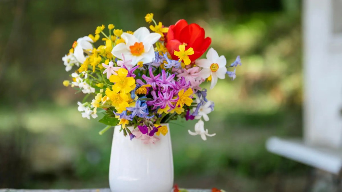Verschiedene Wildblumen in einer weißen Vase stehen draußen auf dem Tisch.