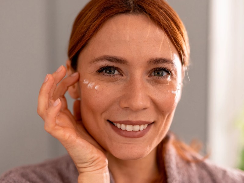 Frau, die sich ein paar Tupfen einer Augencreme auf die Schl&auml;fen auftr&auml;gt.