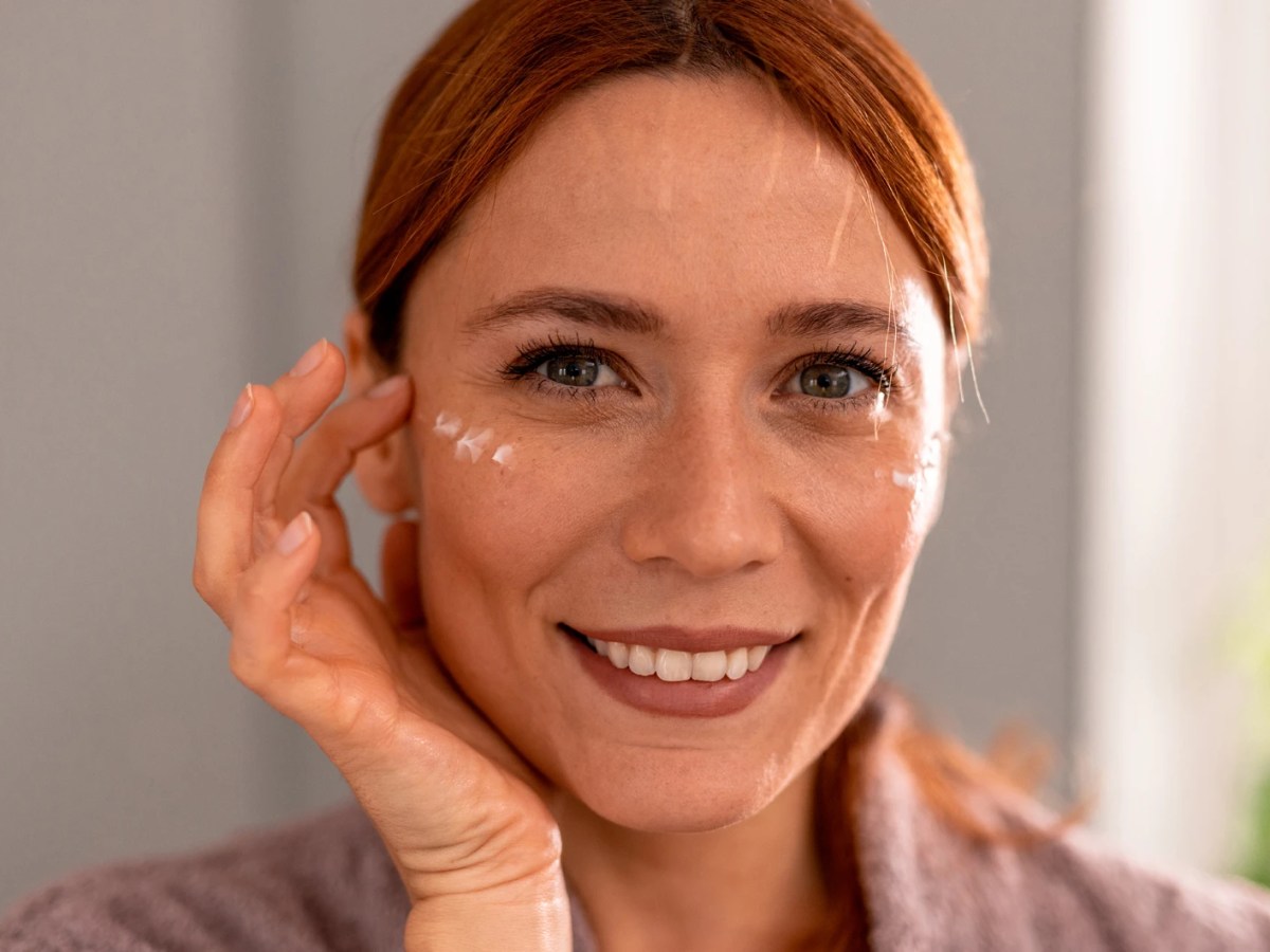 Frau, die sich ein paar Tupfen einer Augencreme auf die Schl&auml;fen auftr&auml;gt.