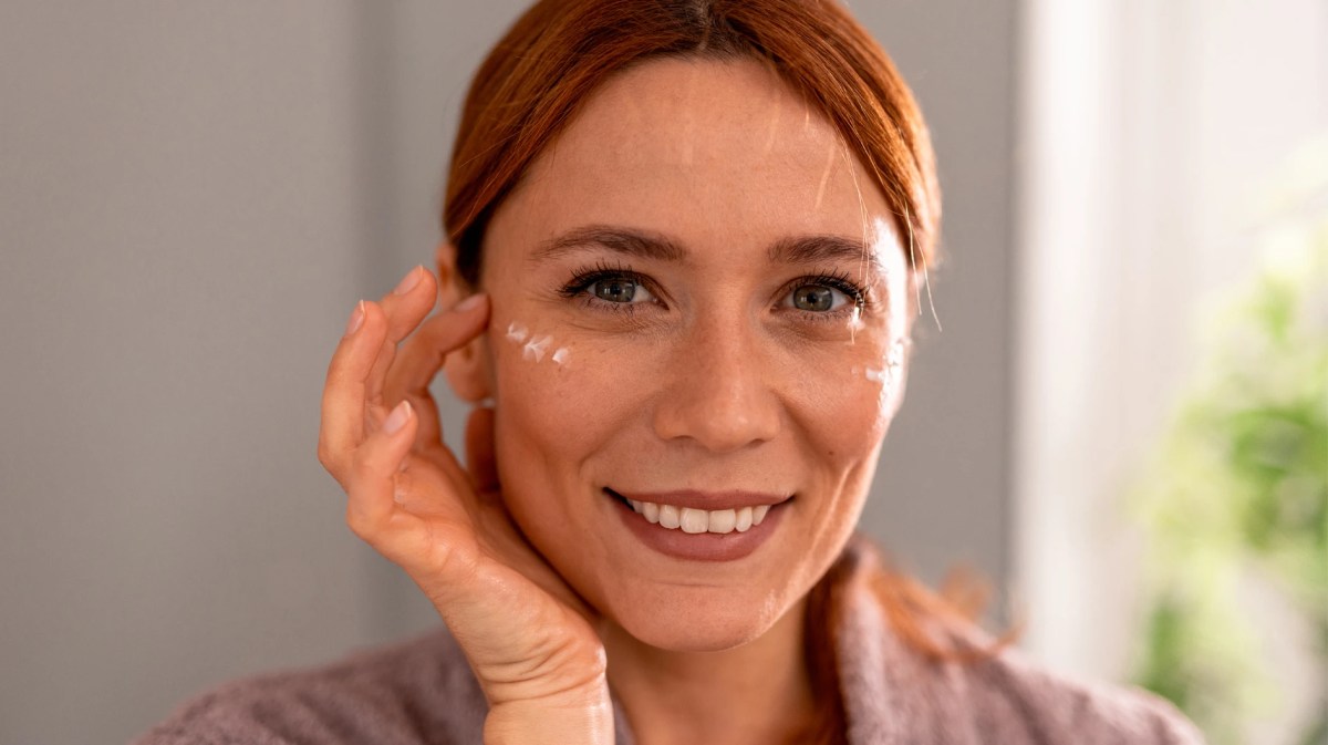 Frau, die sich ein paar Tupfen einer Augencreme auf die Schläfen aufträgt.
