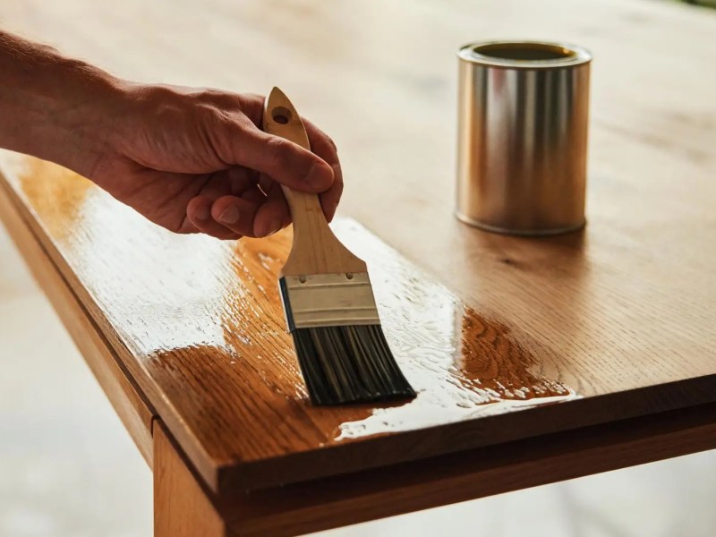 Person lasiert mit einer Lasur einen Holztisch.