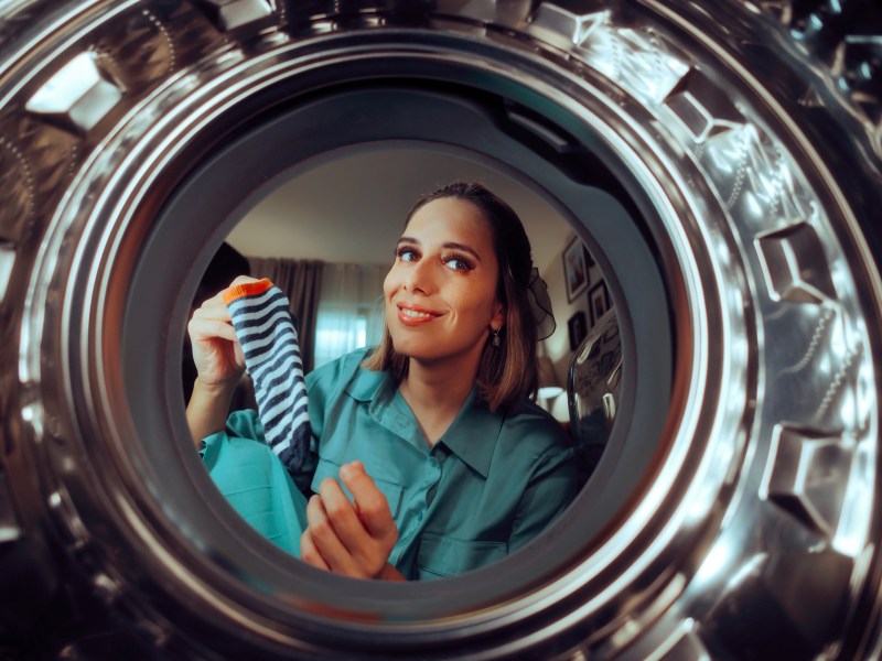 Frau guckt in eine leere Waschmaschine und hält eine Socke in der Hand