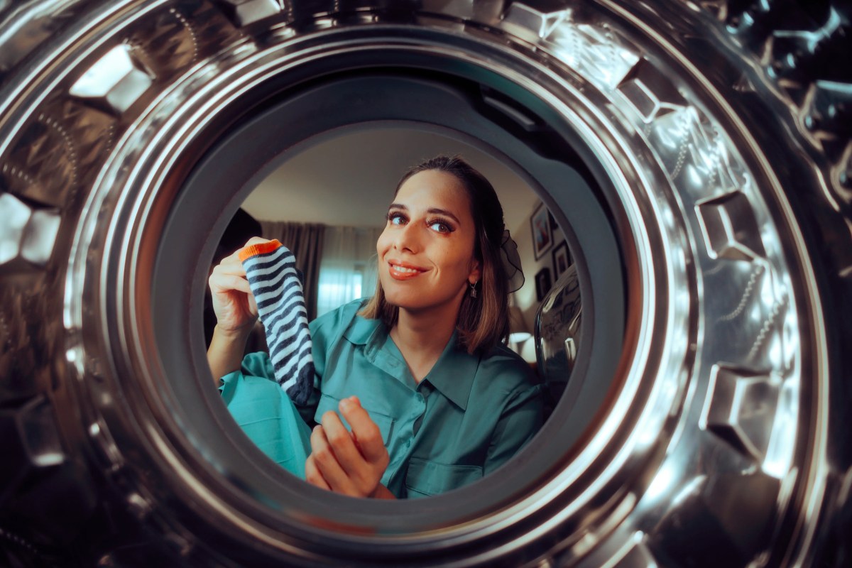 Frau guckt in eine leere Waschmaschine und hält eine Socke in der Hand