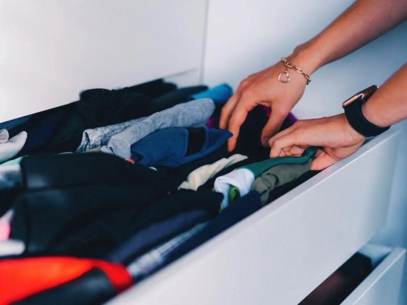 Frau greift in eine Kleidungsschublade, in der gefaltete Kleidung, vor allem Unterwäsche und Socken, liegen.