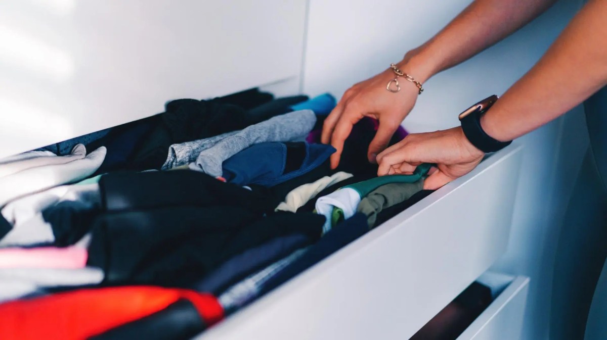 Frau greift in eine Kleidungsschublade, in der gefaltete Kleidung, vor allem Unterwäsche und Socken, liegen.