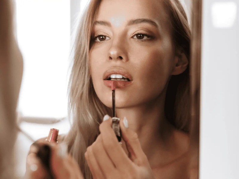 Junge Frau trägt Lippenstift auf.