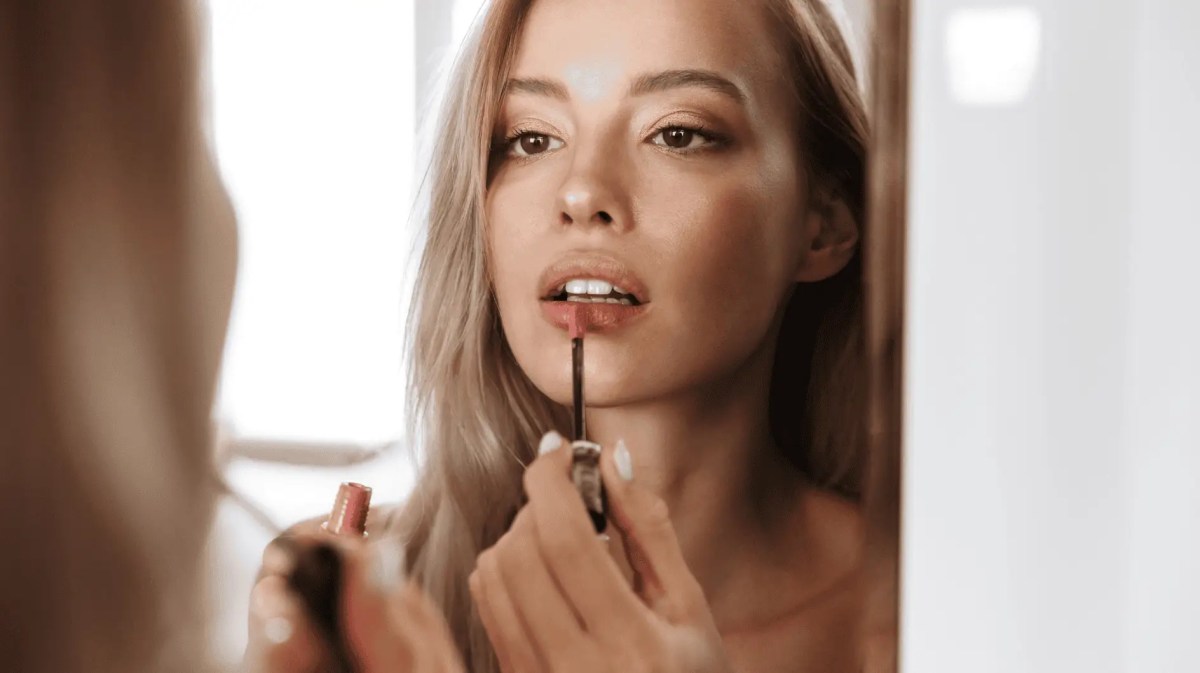 Junge Frau trägt Lippenstift auf.