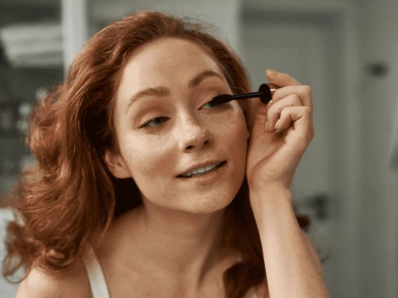 Junge Frau mit roten Haaren trägt Mascara auf.