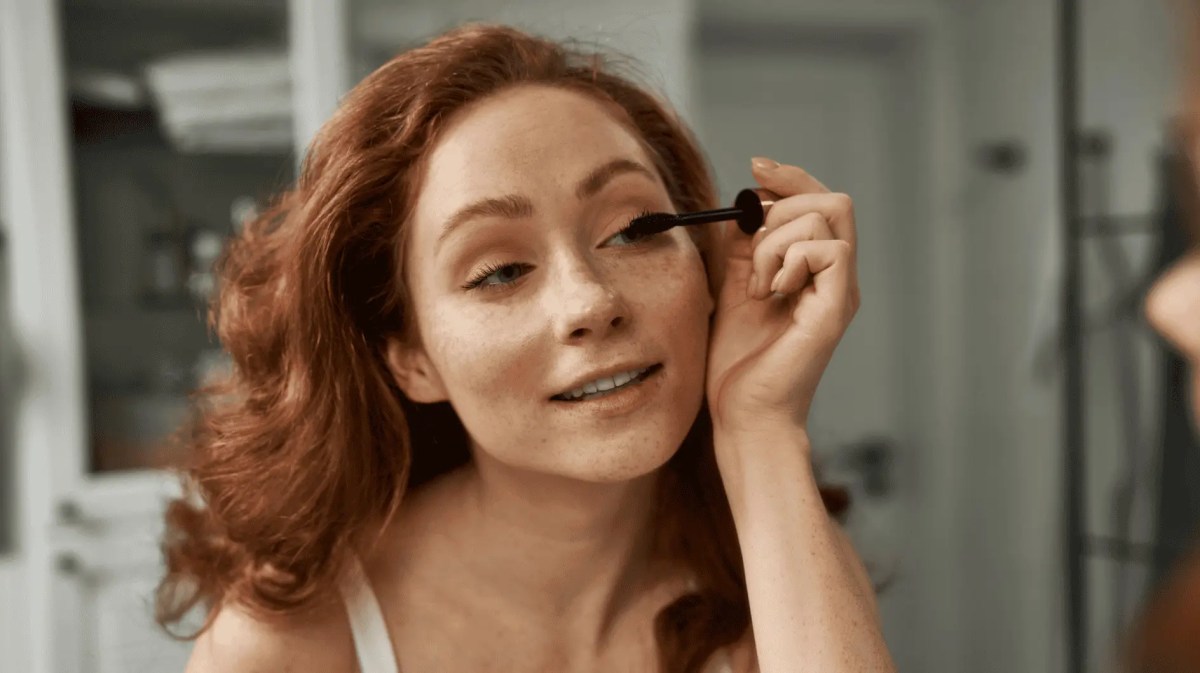 Junge Frau mit roten Haaren trägt Mascara auf.