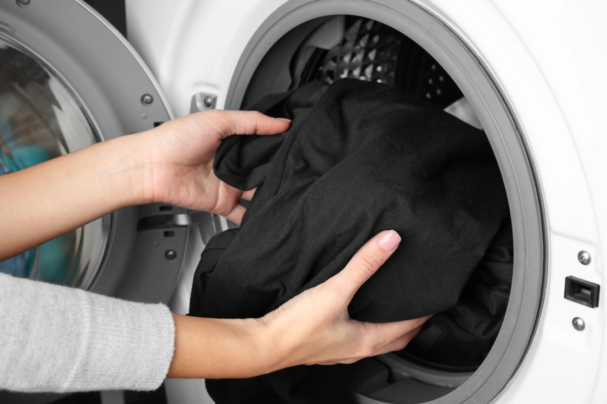 Nahaufnahme von Frauenhänden, die schwarze Wäsche in die Waschmaschine packen