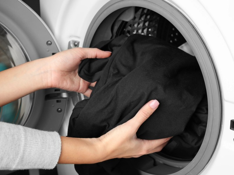 Nahaufnahme von Frauenhänden, die schwarze Wäsche in die Waschmaschine packen