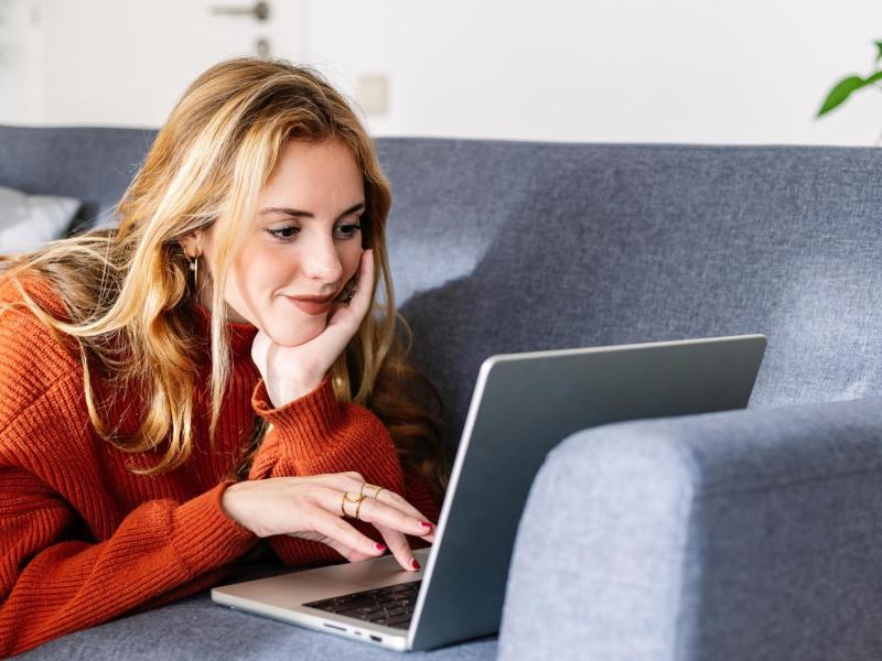 Junge Frau liegt auf der Couch mit ihrem Laptop.