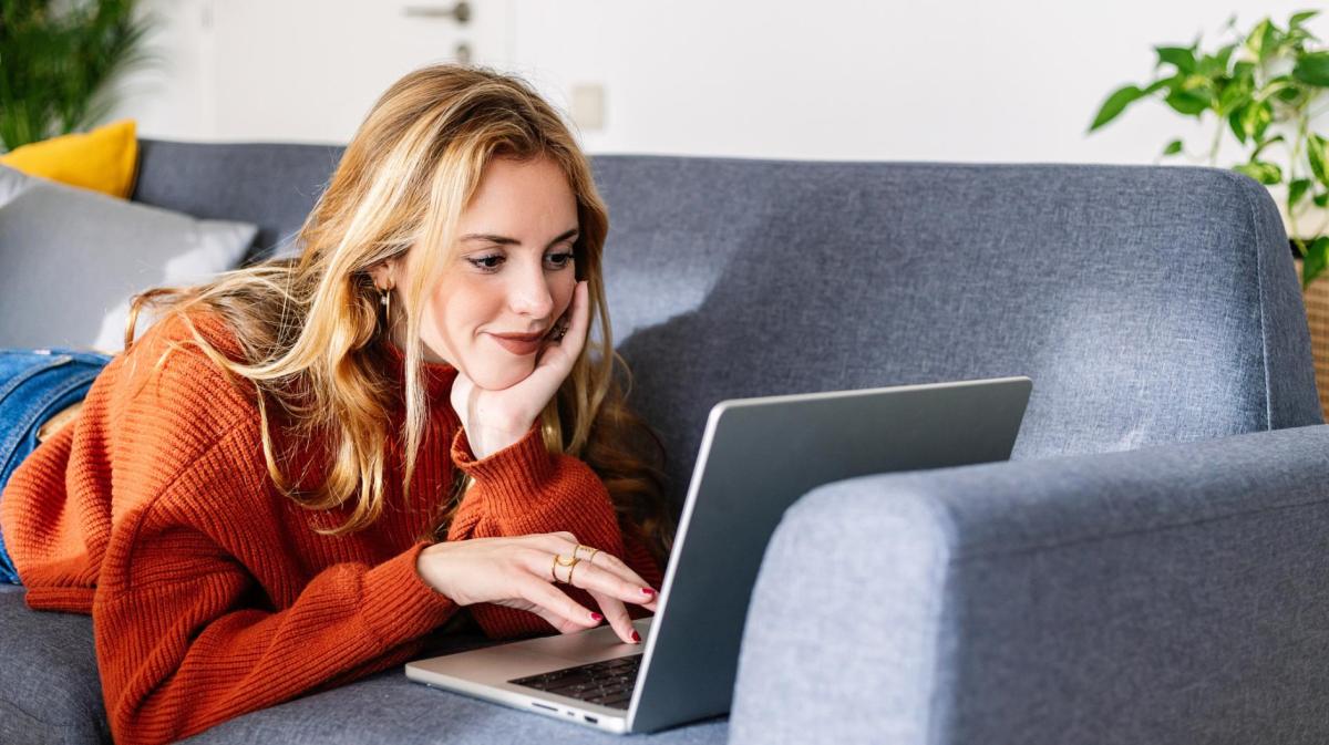 Junge Frau liegt auf der Couch mit ihrem Laptop.