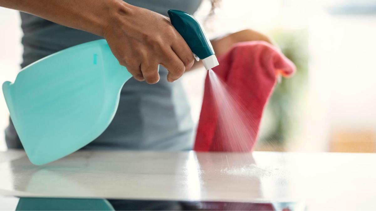 Frau sprüht Wasser auf eine Küchenoberfläche und hält einen Lappen in der Hand.