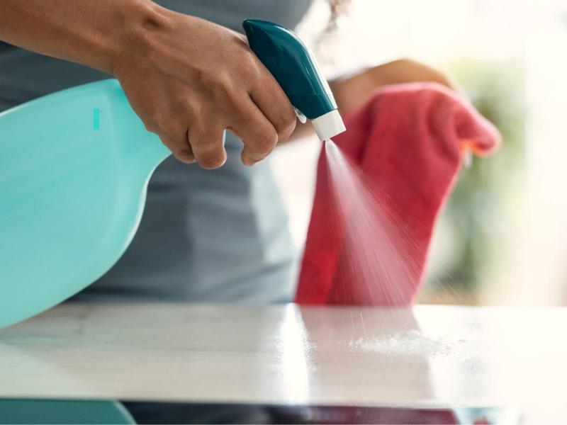 Frau sprüht Wasser auf eine Küchenoberfläche und hält einen Lappen in der Hand.