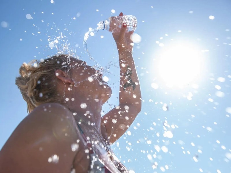 Frau gießt sich an einem sonnigen Tag Wasser über den Kopf.