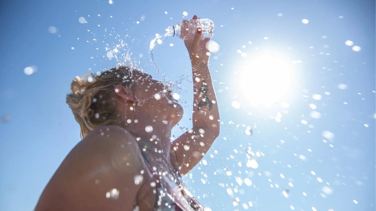 Frau gießt sich an einem sonnigen Tag Wasser über den Kopf.