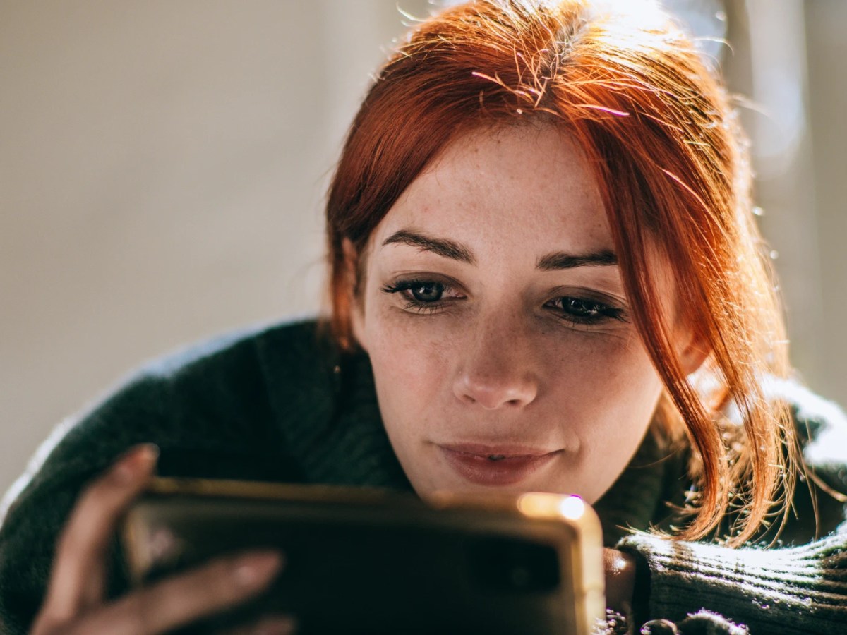Frau mit roten Haaren und einem Smartphone in der Hand