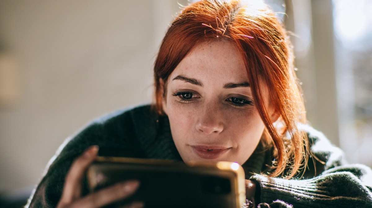 Frau mit roten Haaren und einem Smartphone in der Hand