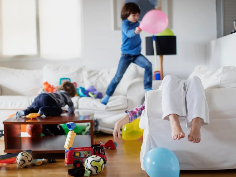 Mutter liegt erschöpft auf der Couch, während ihre Kinder wild drumherum hüpfen